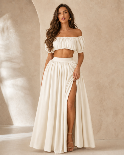 Woman wearing an ivory off shoulder crop top and flowing high slit maxi skirt set front view